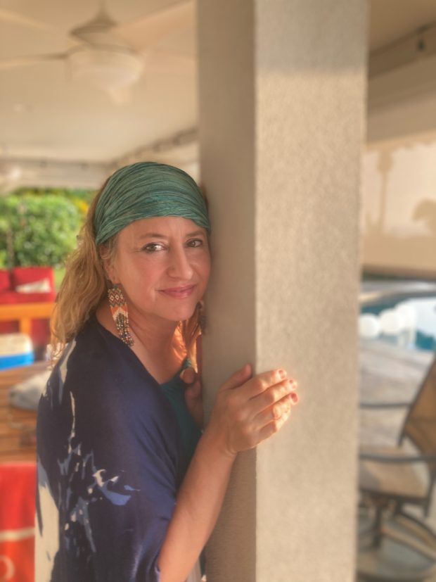 Karen Loudon leaning against a lanai post, wearing a green headscarf and looking to camera
